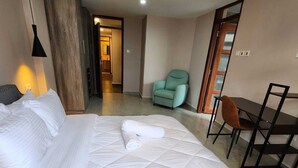A hotel room with a large bed, a desk, a chair, and a door leading to another room.