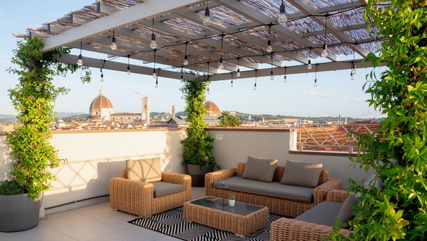 A rooftop terrace with wicker furniture, potted plants, and a view of a cityscape including a dome and tower. - Il Santo Stays (Florence)