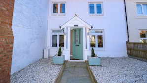 A white two-story house with a green door, two windows on the ground floor, and a small garden area with gravel and two potted plants. - 1 Star Cottages (Freshwater)