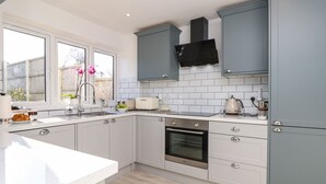 A modern kitchen with grey cabinets, a built-in oven, and a window with a view of the outside. - 1 Star Cottages (Freshwater)