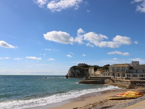 A coastal scene with a sandy beach, rocky cliffs, and a building with a flag.