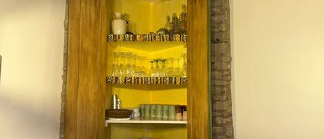 A wooden cabinet with shelves holding glassware, plates, and cups.