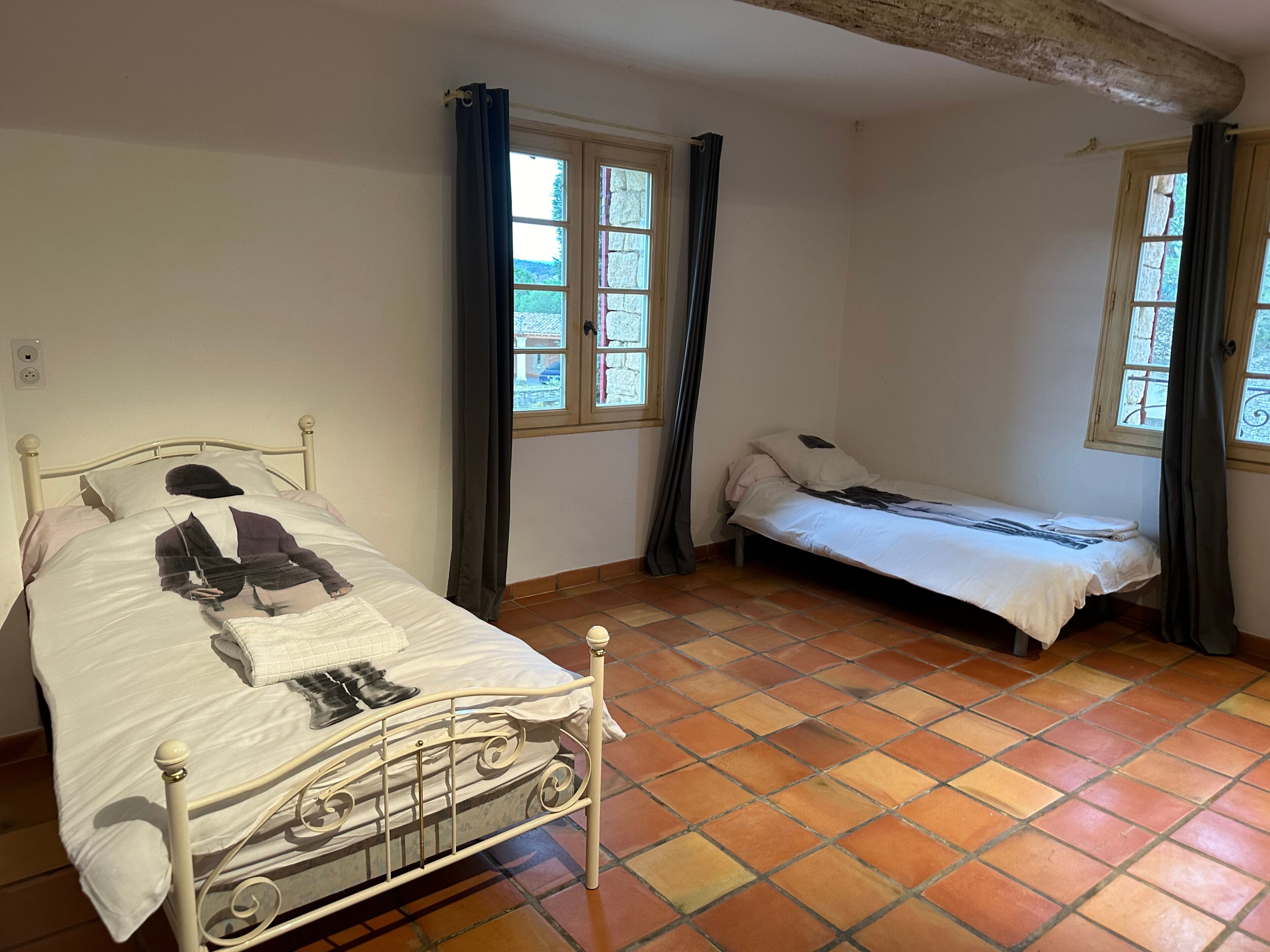 Una habitación con dos camas, piso de baldosas y ventanas con cortinas.
