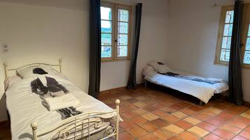 Una habitación con dos camas, piso de baldosas y ventanas con cortinas.