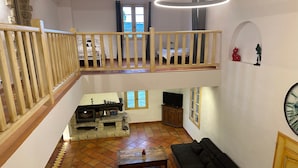 Un vaste espace de vie doté d’un haut plafond, d’un escalier en bois, d’une cheminée, d’un canapé et d’un téléviseur.