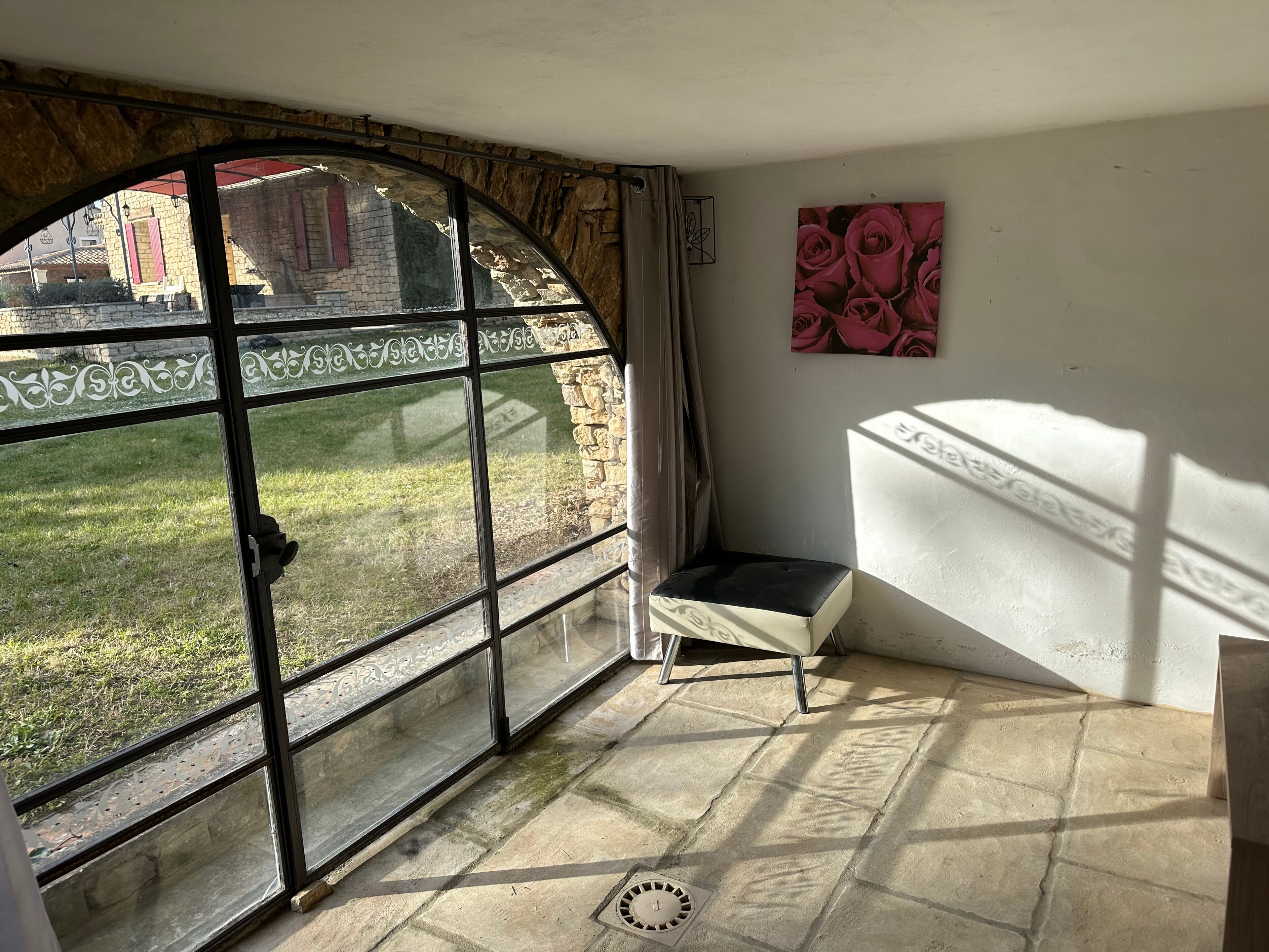 A room with a stone floor, a window with decorative glass, a bench, and a painting of roses.