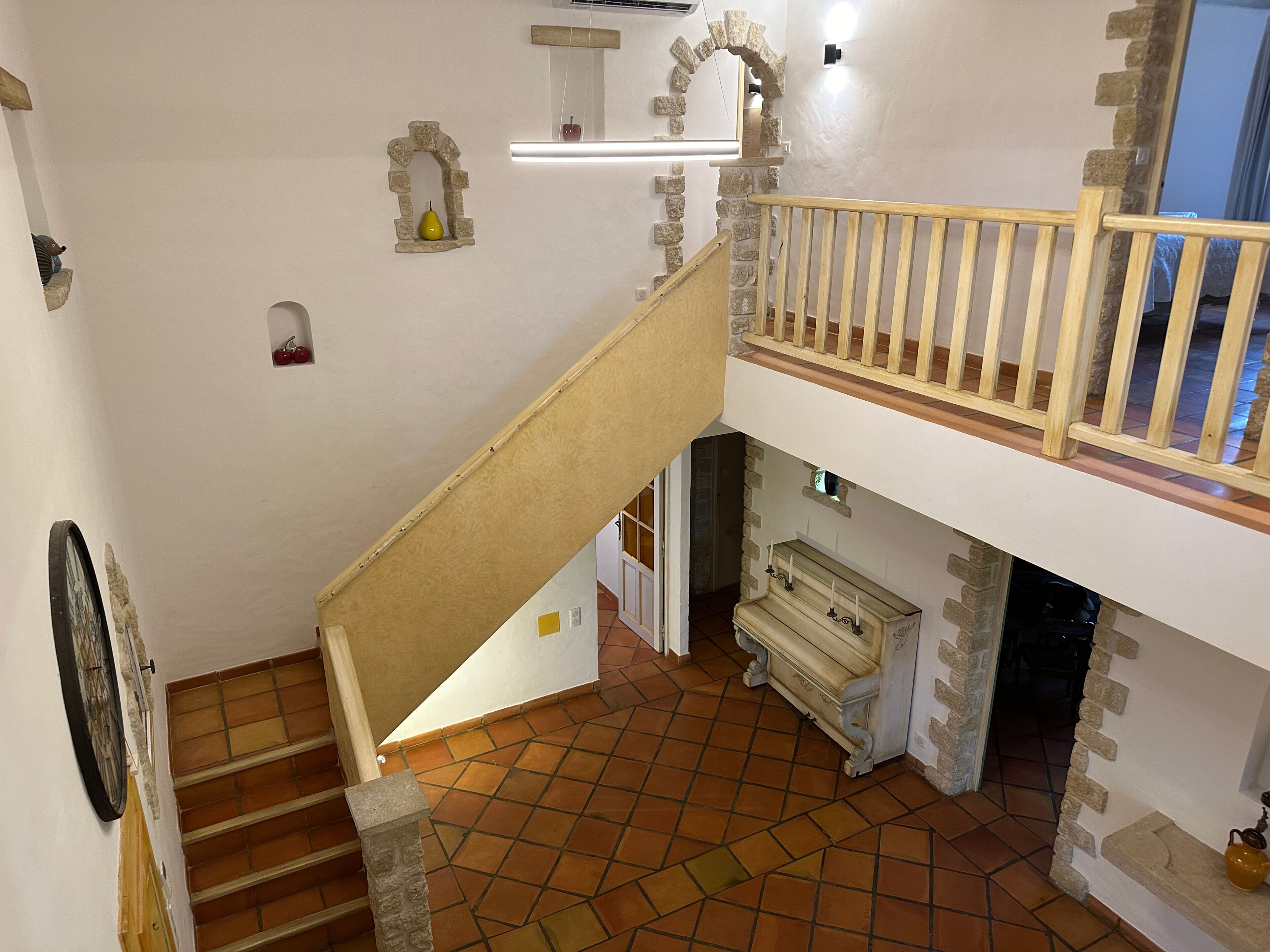 Una escalera con barandilla de madera que lleva a un balcón en el segundo piso con balaustrada de piedra.