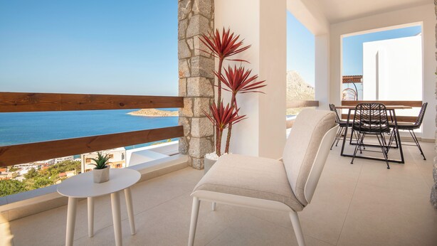 A balcony with a view of the sea, a stone pillar, a potted plant, a white chair, and a table with chairs.
