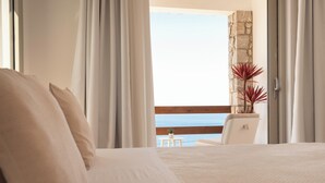 A bedroom with a large bed, a view of the sea through a balcony, and a stone wall.