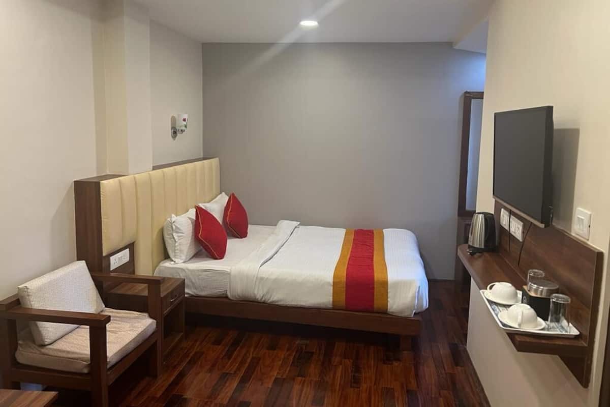 Una habitación de hotel con cama, sillón, televisor y una bandeja con tazas y tetera.