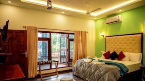 A bedroom with a large bed, a wooden desk, and a view of the outdoors through a sliding door. - FIGO BEACH RESORT (Varkala)