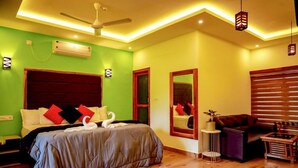 A bedroom with a large bed, a ceiling fan, a small round ottoman, and a wooden side table. - FIGO BEACH RESORT (Varkala)