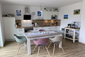 Een moderne keuken met witte kasten, een houten aanrecht, een eettafel met vier stoelen en een magnetron.