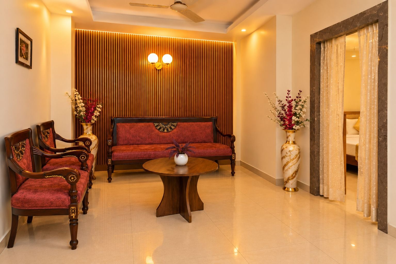 Um hall de hotel com um conjunto de sofás, cadeiras, uma mesa redonda e um vaso com flores.