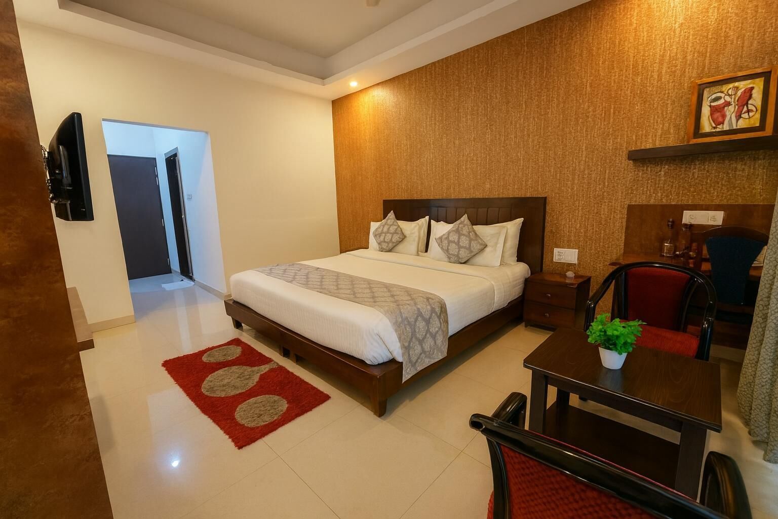 A hotel room with a bed, a desk, a chair, a TV, and a red rug.
