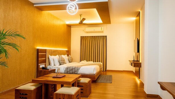 Una habitación de hotel moderna con cama, mesita de noche, lámpara y una pequeña zona de estar con otomanas.