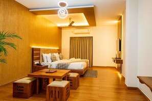 A modern hotel room with a bed, bedside table, lamp, and a small seating area with ottomans. - HOTEL ZION INN (Varanasi)