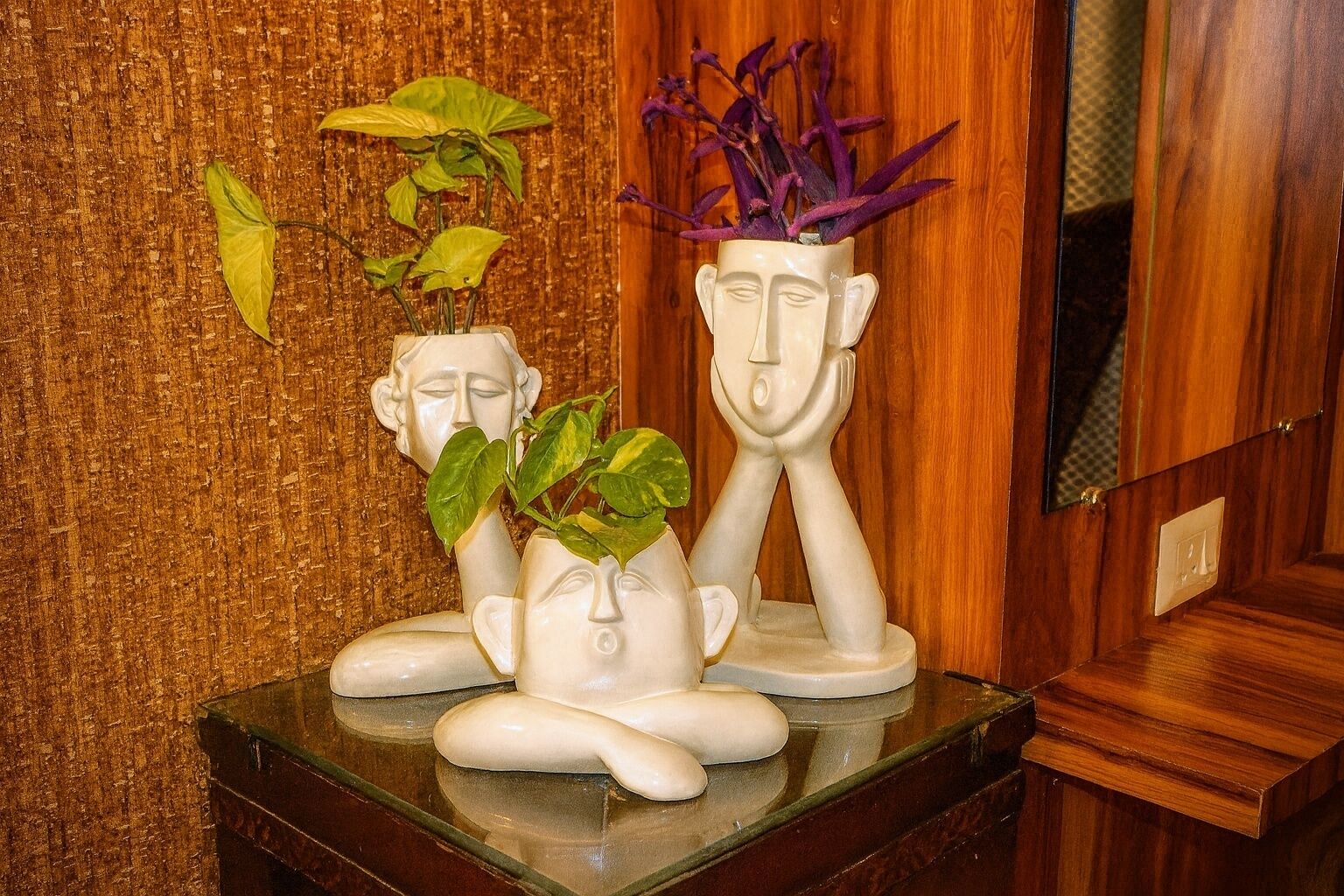 A sculpture of three figures with plants on a wooden surface.