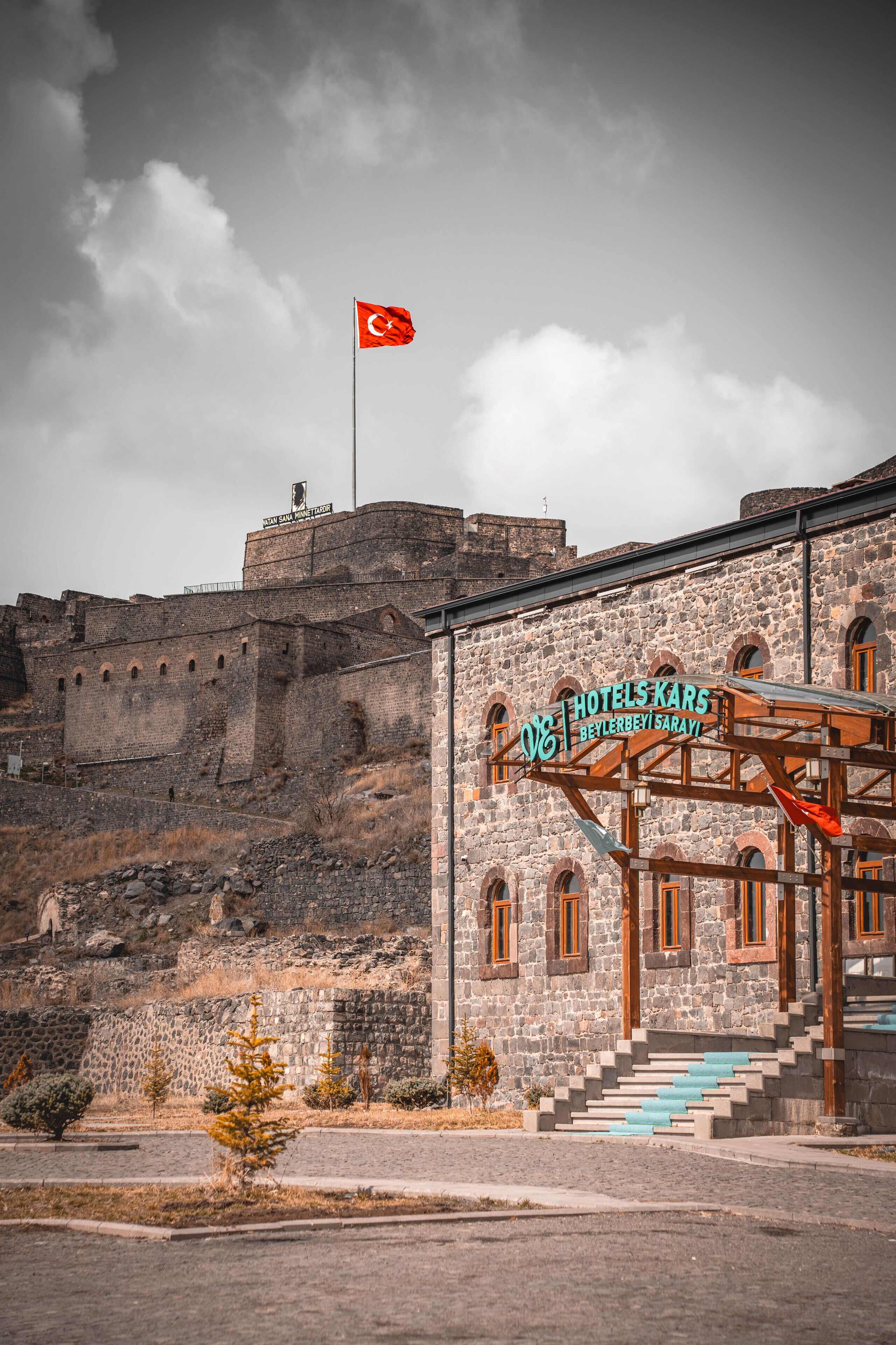 A hotel with a stone facade, a flag, and a sign reading "HOTELS KARS BEYLERBEY SARAY".