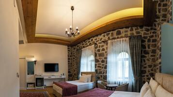 A bedroom with two beds, a desk, a television, and a stone wall.