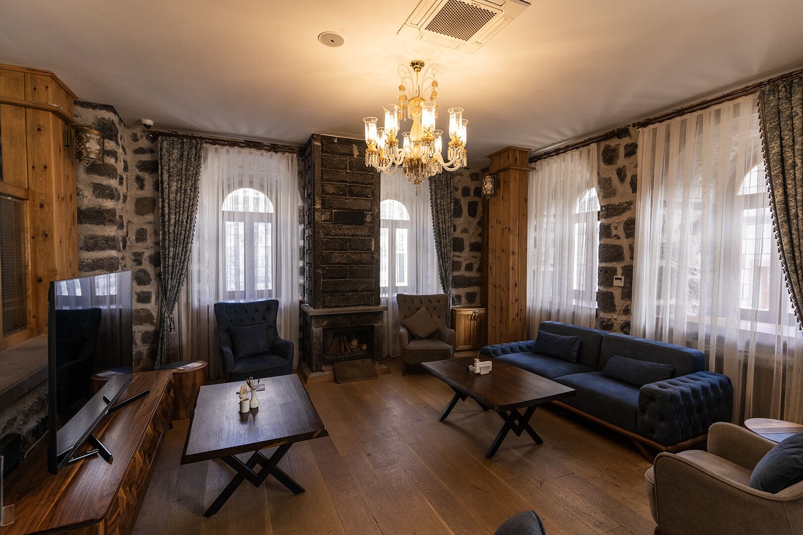 A cozy living room with a stone fireplace, wooden furniture, and a chandelier.