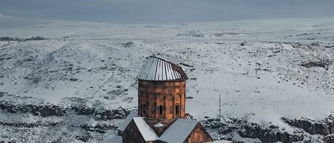 Una iglesia cubierta de nieve con un campanario y un edificio adyacente más pequeño, rodeada por un extenso paisaje nevado.