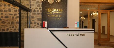 A reception desk with a sign for "VE KARS Hotels Beylerbeyi Sarayı" and "VILAYETLER EVI 'Evimiz Hakkediniz'".