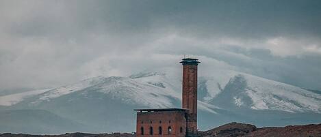 Una torre de ladrillo solitaria sobre una colina yerma, con una montaña nevada al fondo.