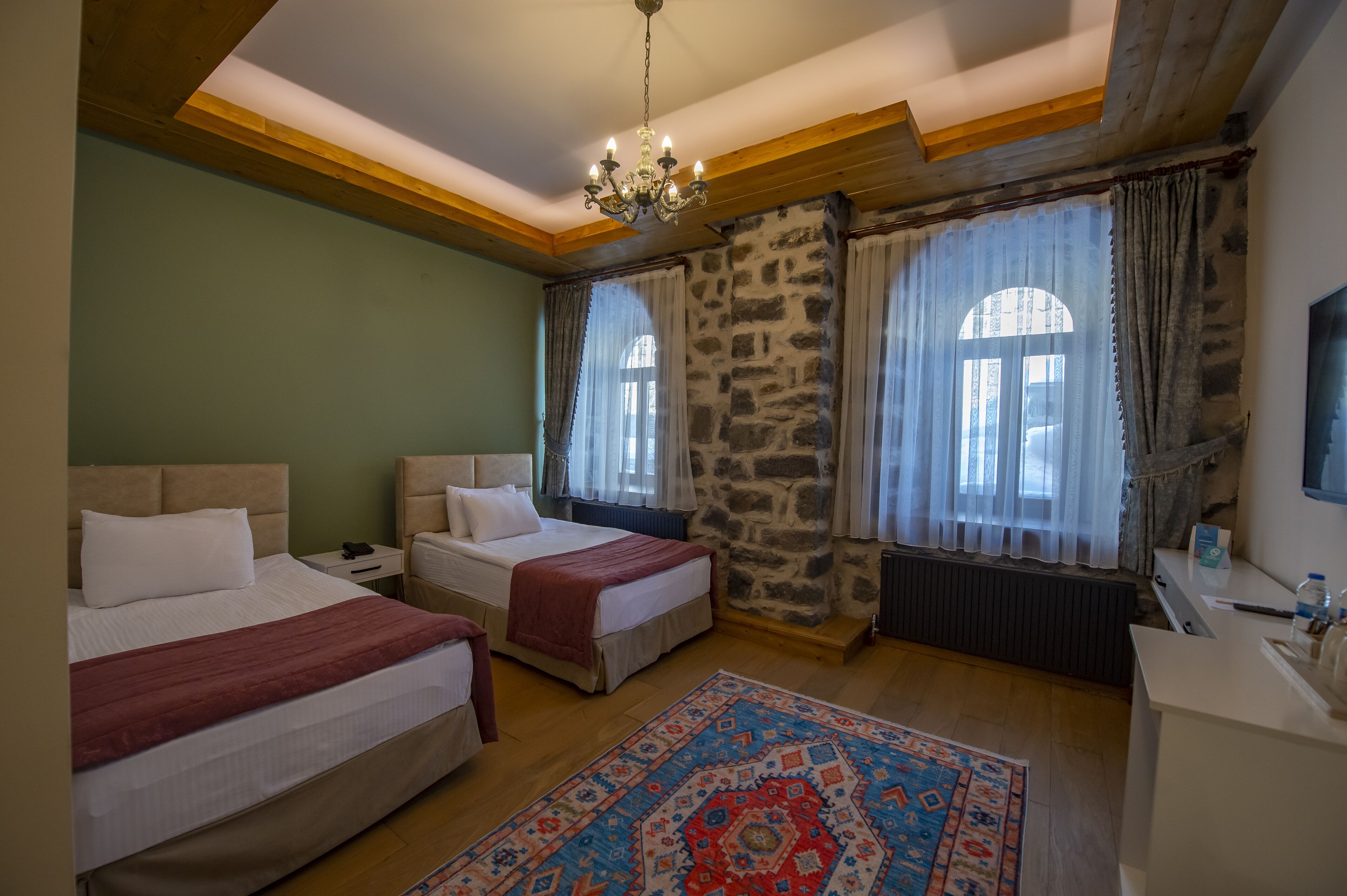A room with two beds, a chandelier, stone walls, and a patterned rug.