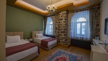 A room with two beds, a chandelier, stone walls, and a patterned rug.