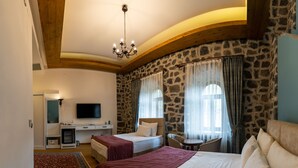Habitación de hotel con dos camas, un escritorio, televisión y pared de piedra.