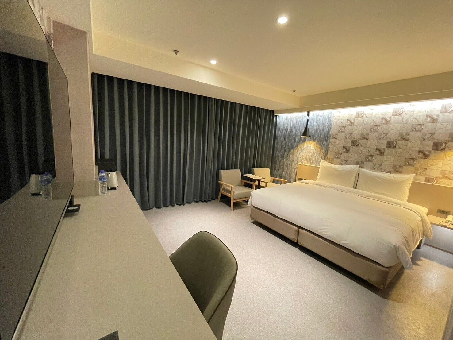 A hotel room with a bed, a desk, a chair, and a small table.