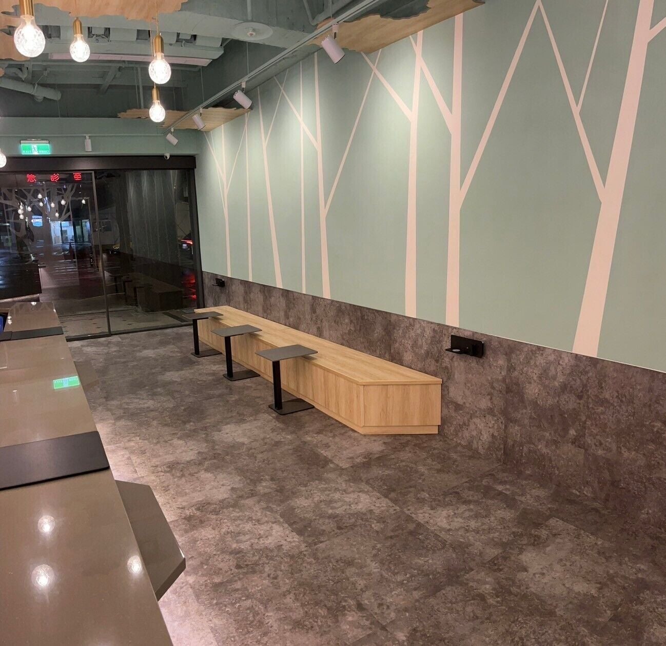 A modern waiting area with a long wooden bench, a glass partition, and a patterned wall.