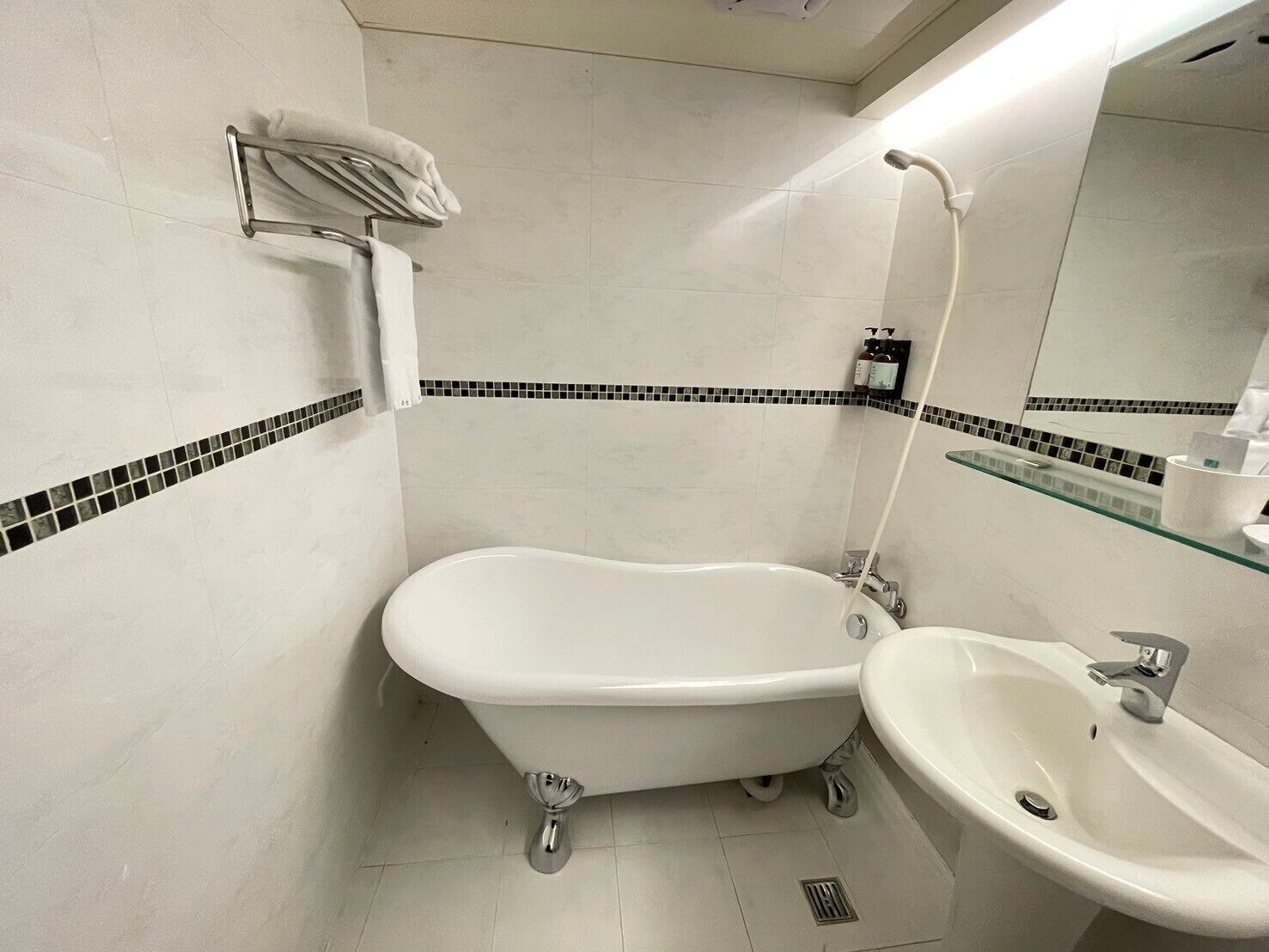 Un baño con una bañera independiente, un lavabo y un estante de vidrio con artículos de aseo.