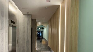 A modern hallway with a marble floor, wooden paneling on one side, and a glass elevator on the other. - SHINSHIN HOTEL (Taipei)