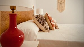 A neatly made bed with a white duvet, a red vase, and patterned pillows. - Casa Mama Carina A (Agüimes)