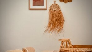 A dining area with a wooden table and chairs, a woven basket on the table, and a wall-mounted macrame piece. - Casa Mama Carina A (Agüimes)