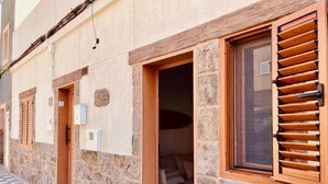 A stone building with a checkered floor, a wooden door, and a window with shutters. - Casa Mama Carina A (Agüimes)