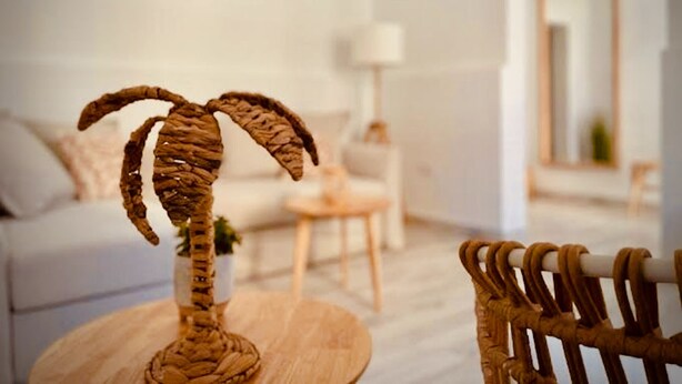 A living room with a wooden coffee table, a wicker chair, a white sofa, and a small plant. - Casa Mama Carina A (Agüimes)