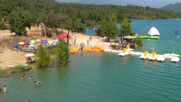 A lakeside beach with canoes, kayaks, and a sailboat.