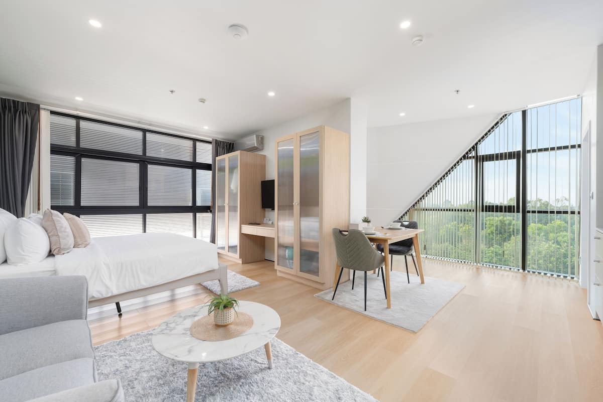 A modern bedroom with a large bed, a desk, and a balcony with a view.