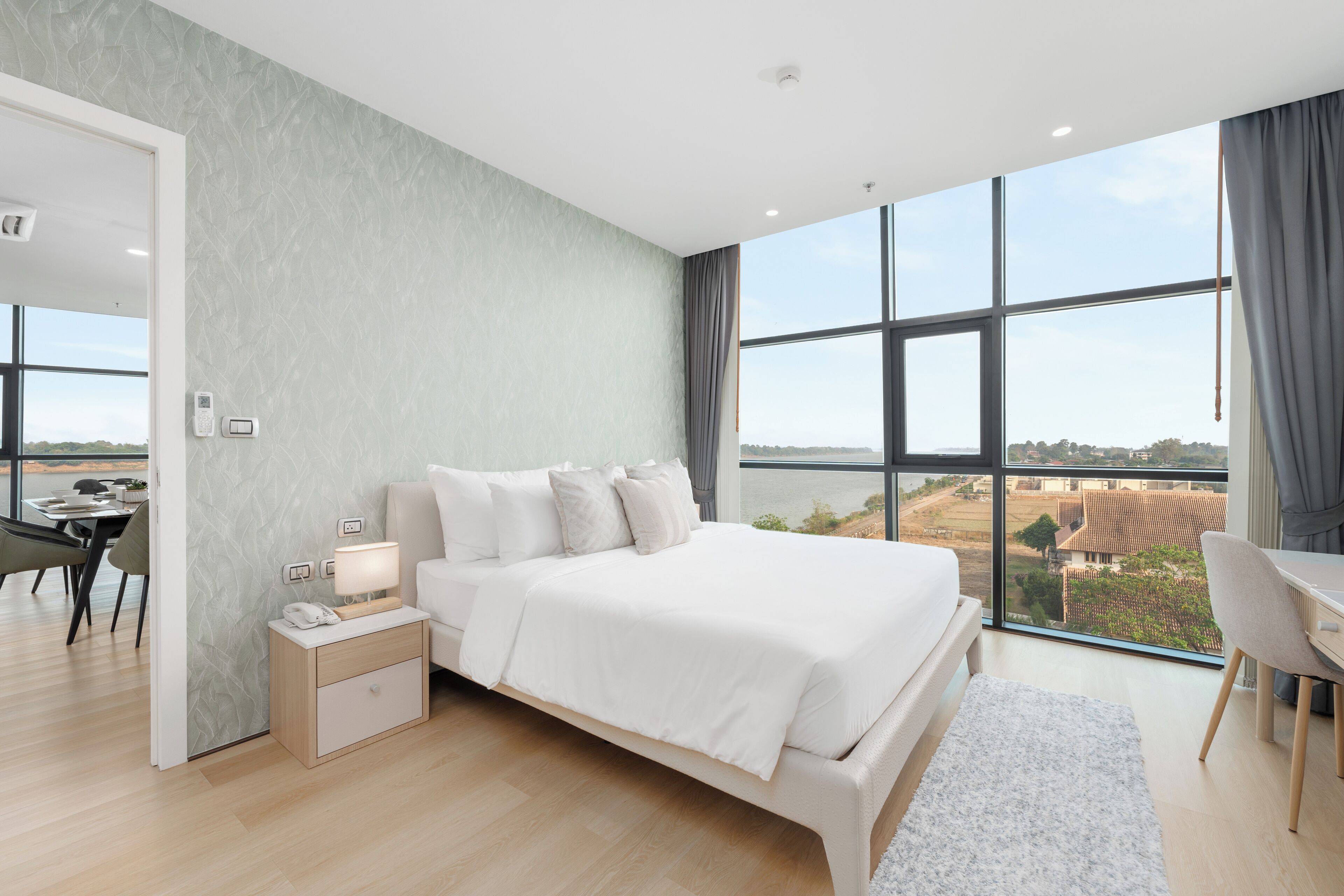 A modern bedroom with a large bed, a desk, and a view of the city.