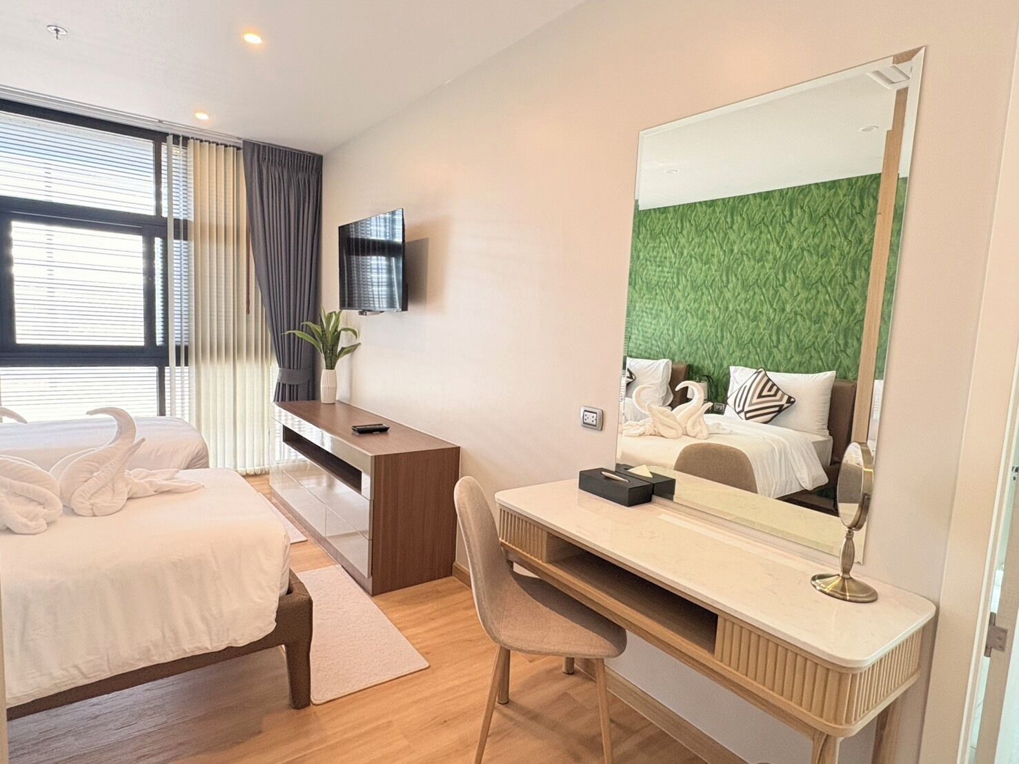 A hotel room with a bed, a desk, a chair, a TV, and a large mirror.