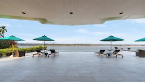 A covered outdoor seating area with four lounge chairs and three green umbrellas, overlooking a body of water. - NAKA-RAJ Escape Hotel (Nakhon Phanom)