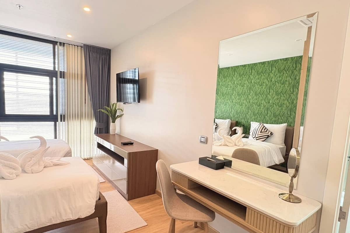 A hotel room with a bed, a desk, a chair, a TV, and a large mirror.