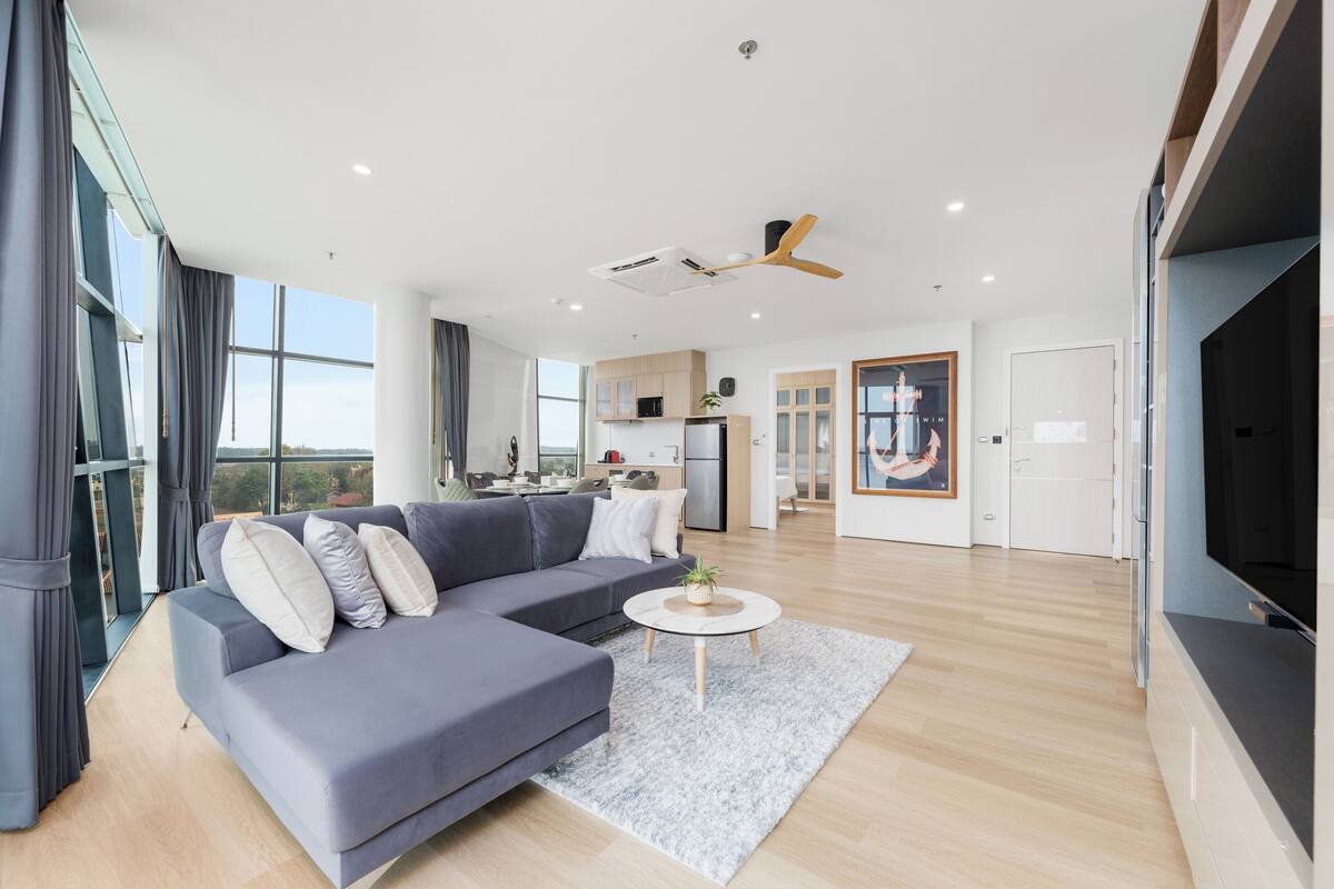 A modern living room with a grey sectional sofa, a round coffee table, and a large window offering a view of the outdoors.
