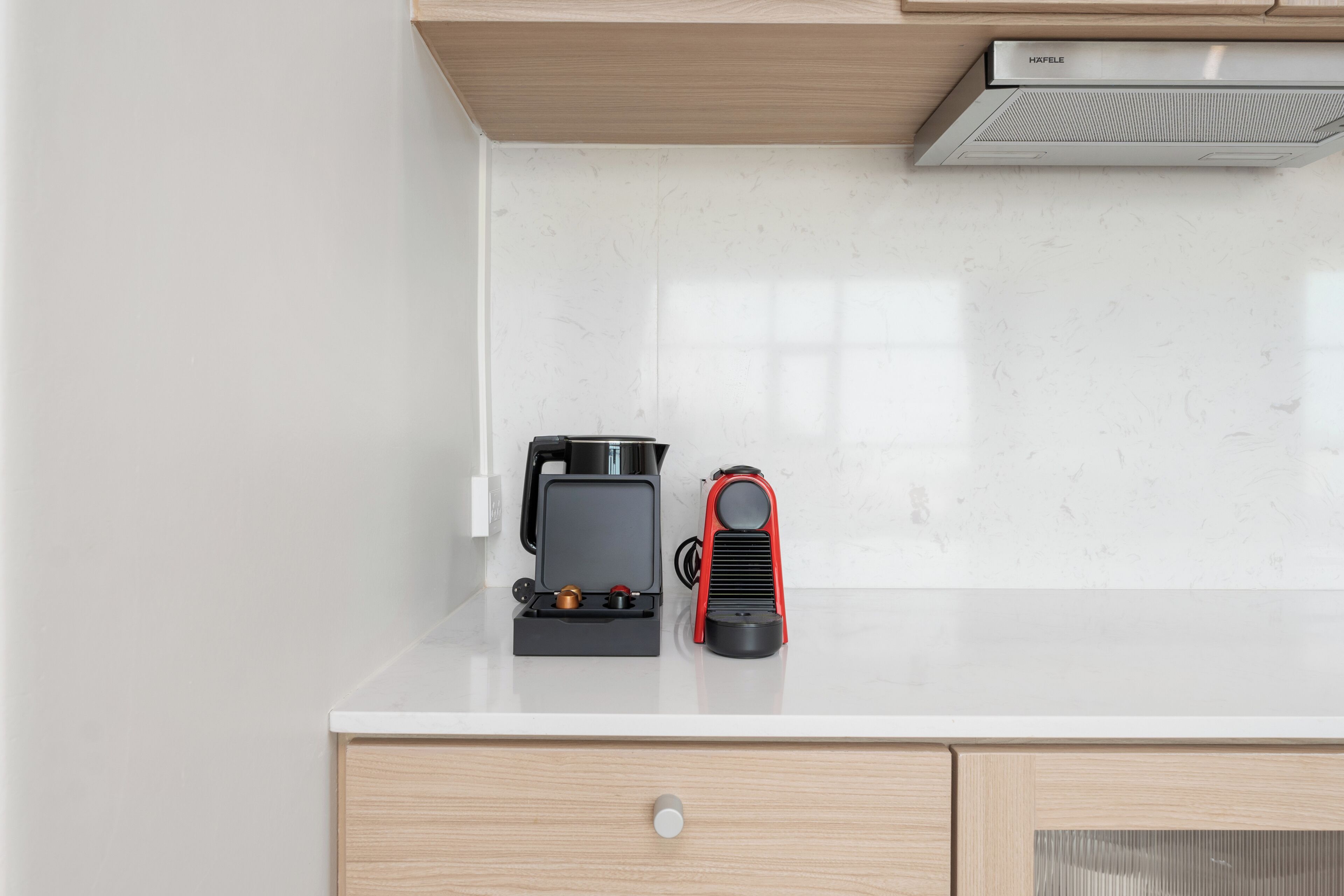 Una cocina con cafetera y un electrodoméstico rojo sobre una encimera blanca.