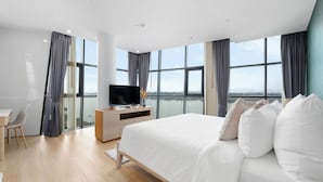 A modern hotel room with a large bed, a TV on a wooden desk, and a view of the water. - NAKA-RAJ Escape Hotel (Nakhon Phanom)