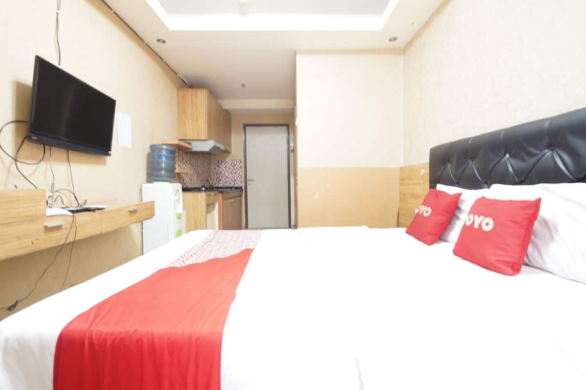 A hotel room with a bed, a TV mounted on the wall, a kitchenette, and a door leading to another room.