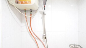 Un chauffe-eau équipé de deux tuyaux, d’une pomme de douche et d’une étagère en métal.